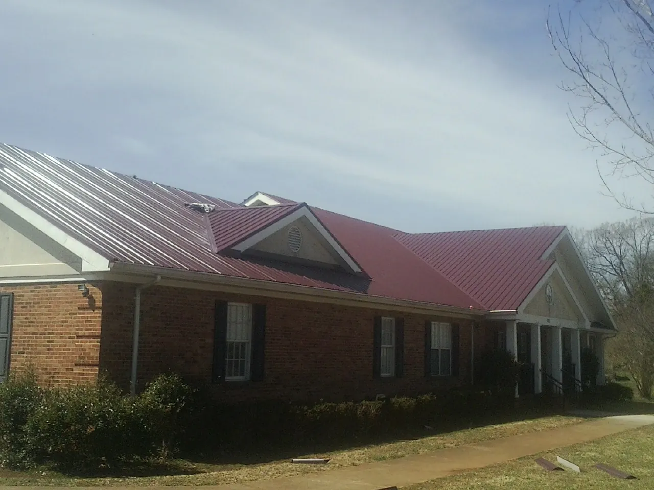 Red metal roof with gabled entries on a long brick building, from a Hail Damage Roof Repair job in Murray